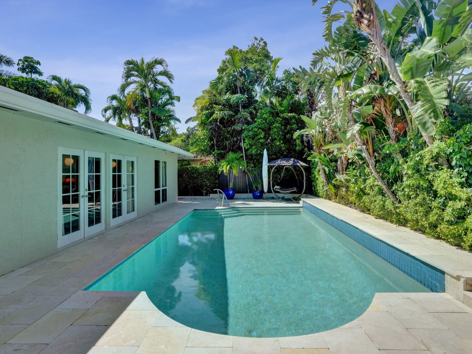 Rectangular swimming pool with a curved entry, surrounded by light-toned pavers, and lush tropical landscaping