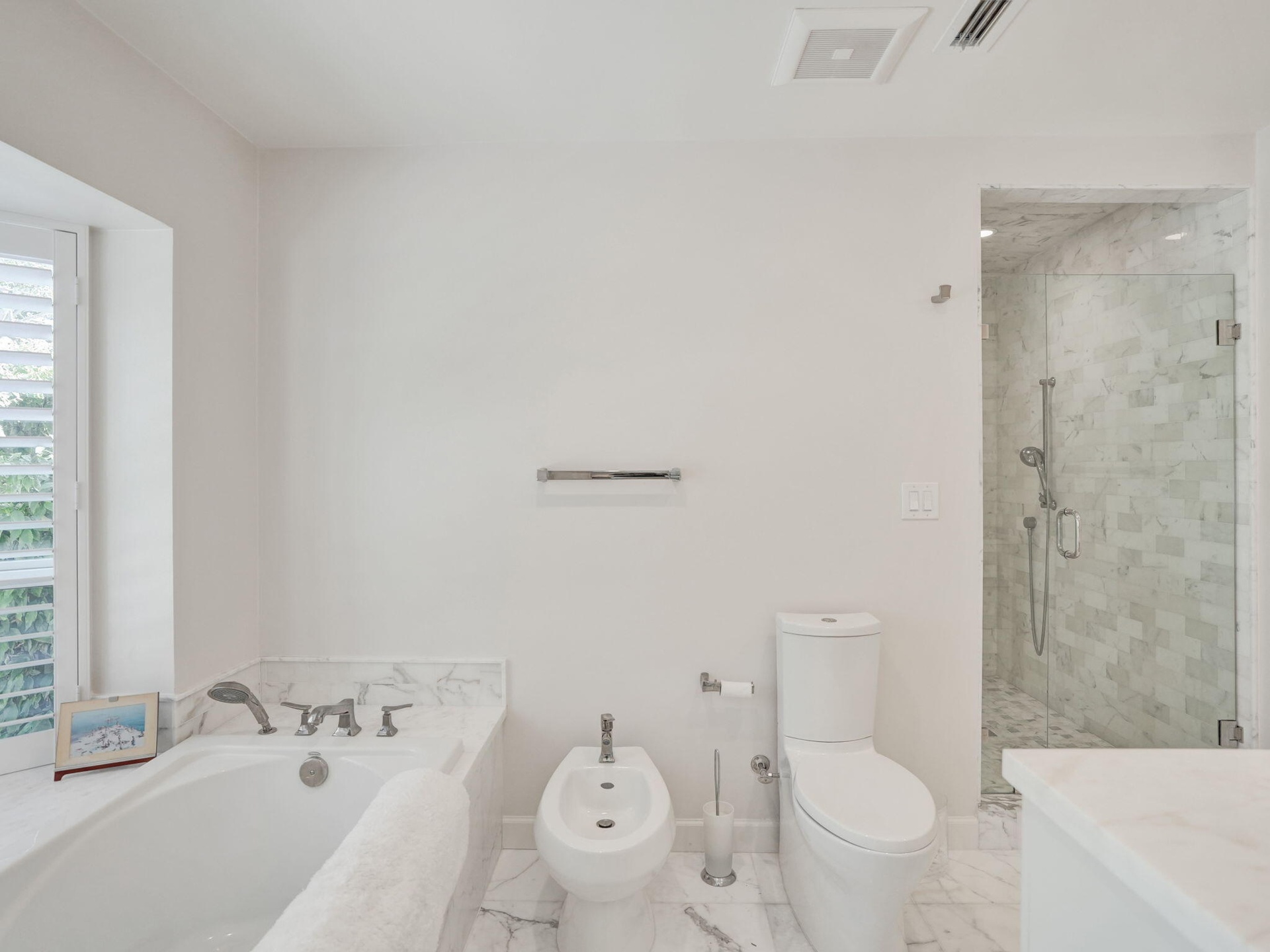 Built-in bathtub with marble surround, glass-enclosed shower with tile surround, bidet, and white wood-finish window shutters