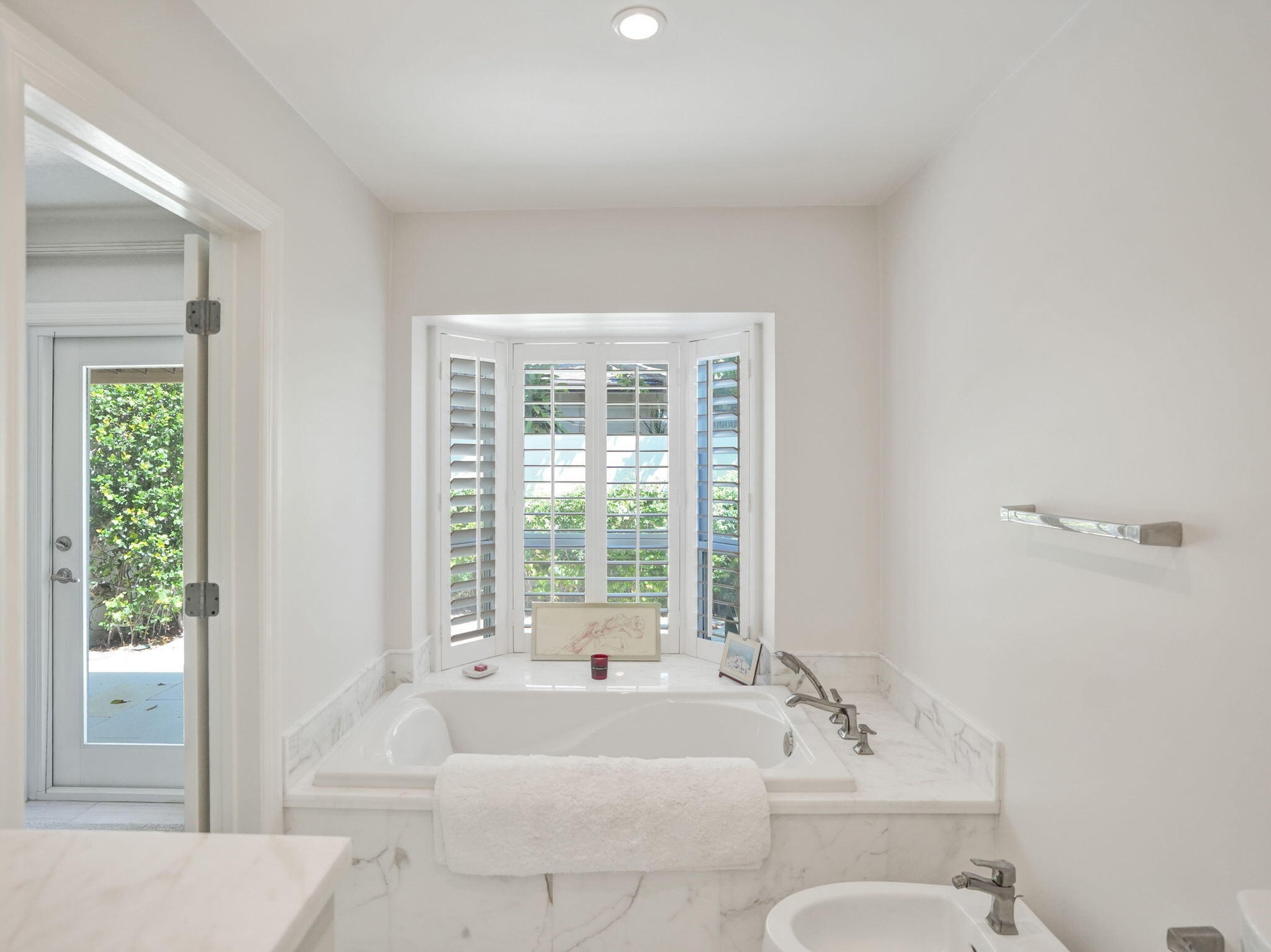 Recessed lighting, bay window with plantation shutters, built-in soaking tub with marble surround, polished chrome fixtures, and bidet
