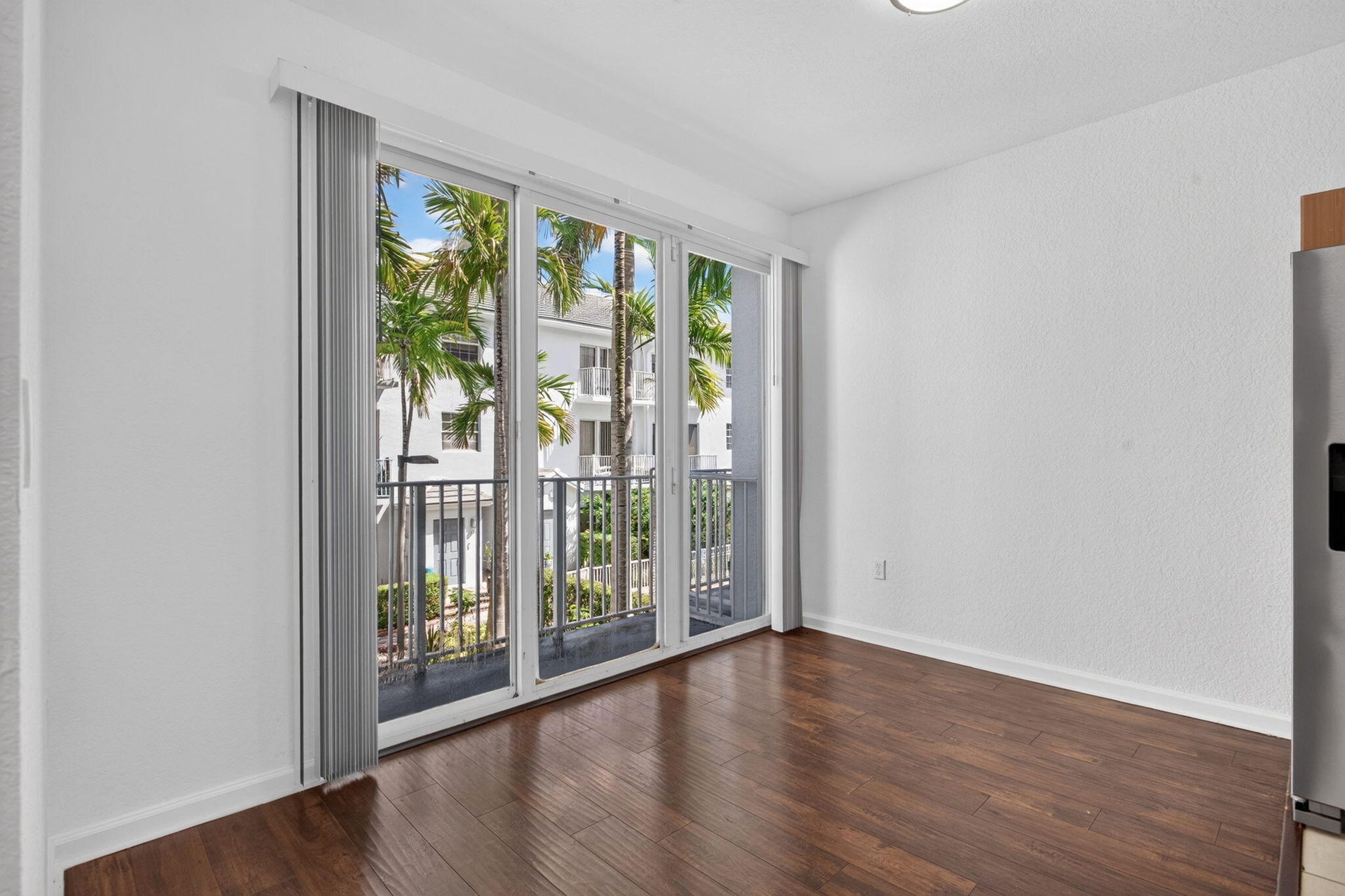 Wood-finish flooring with floor-to-ceiling sliding glass doors opening to a balcony with metal railings