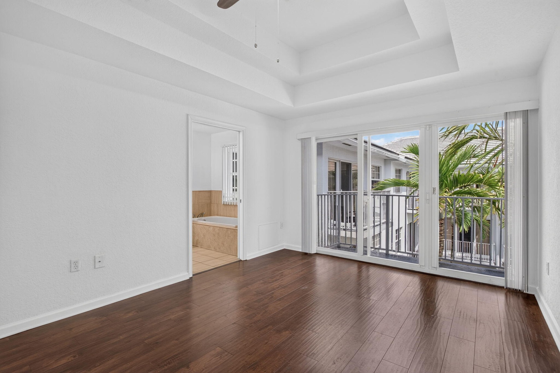 Tray ceiling, wood-finish flooring, sliding glass door, private balcony with black railings, and a built-in tub
