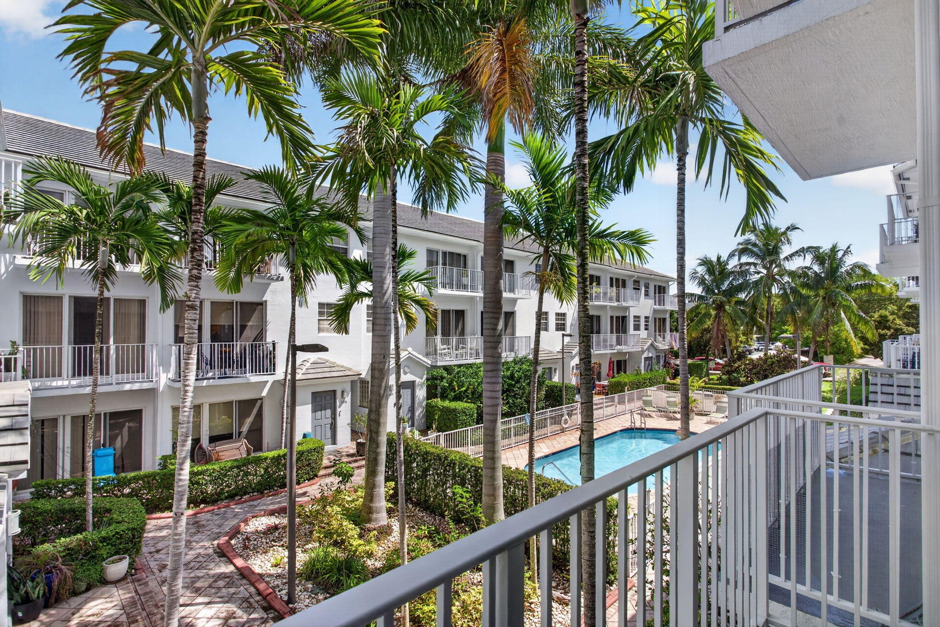 Balcony overlooking courtyard with palm trees, swimming pool, and multiple-story residential buildings