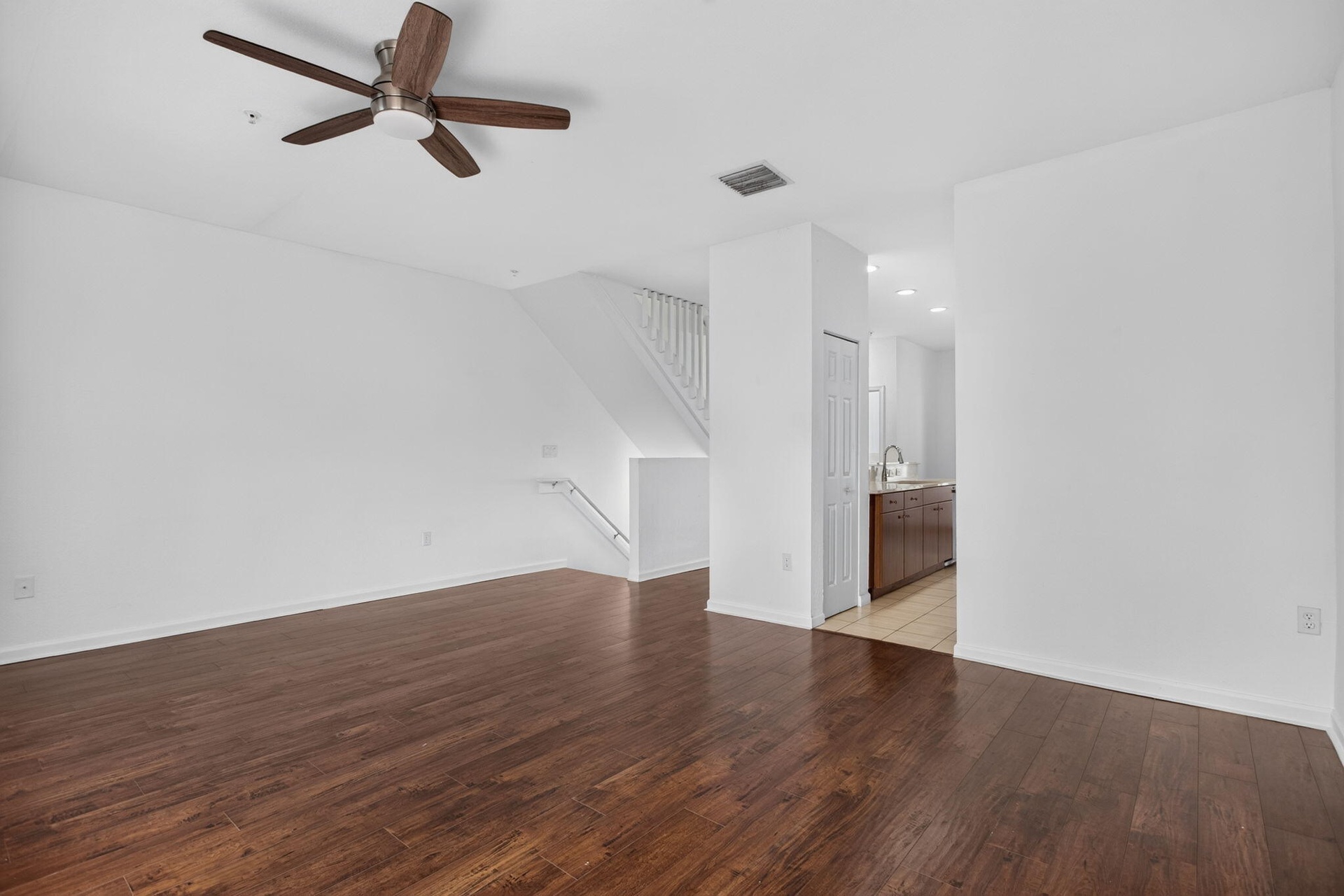 Wood-finish flooring throughout, white painted walls, and a ceiling fan with integrated lighting