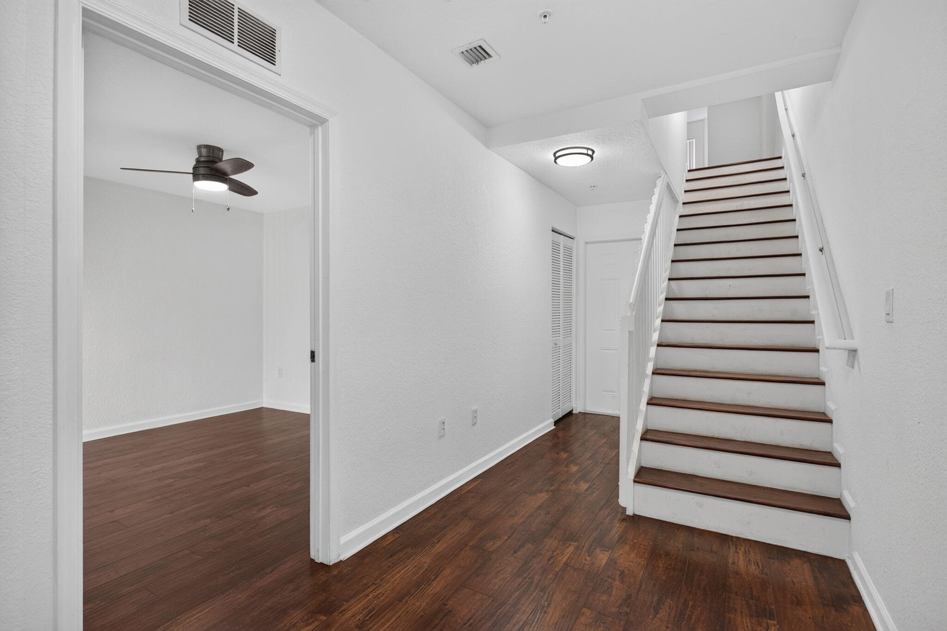 Wood-finish flooring throughout, white walls, and a staircase with white risers and dark wood treads