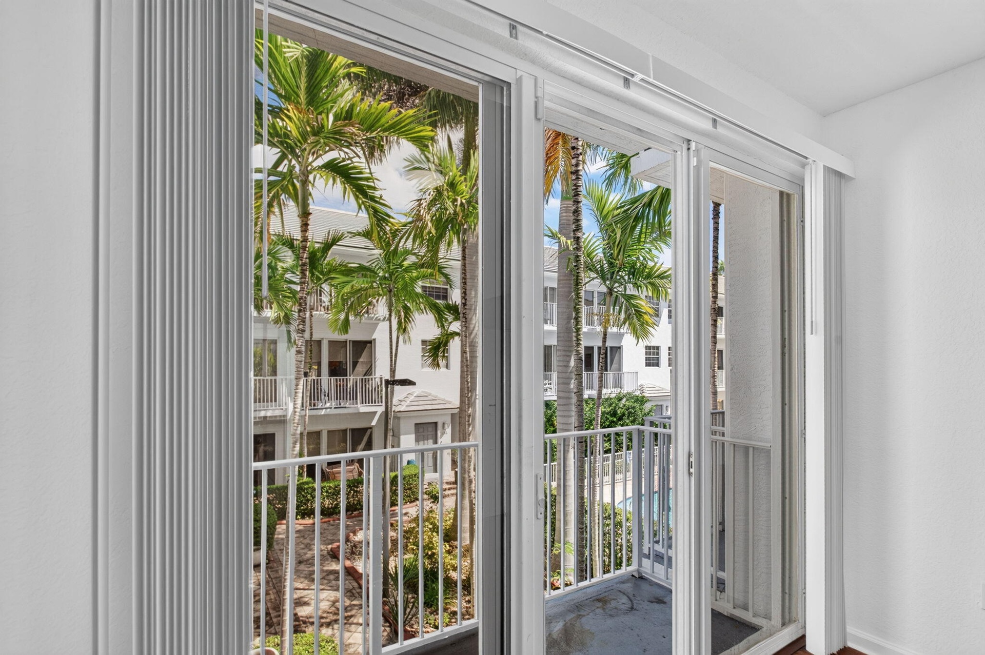 Sliding glass doors with vertical blinds open to a private balcony with a white metal railing