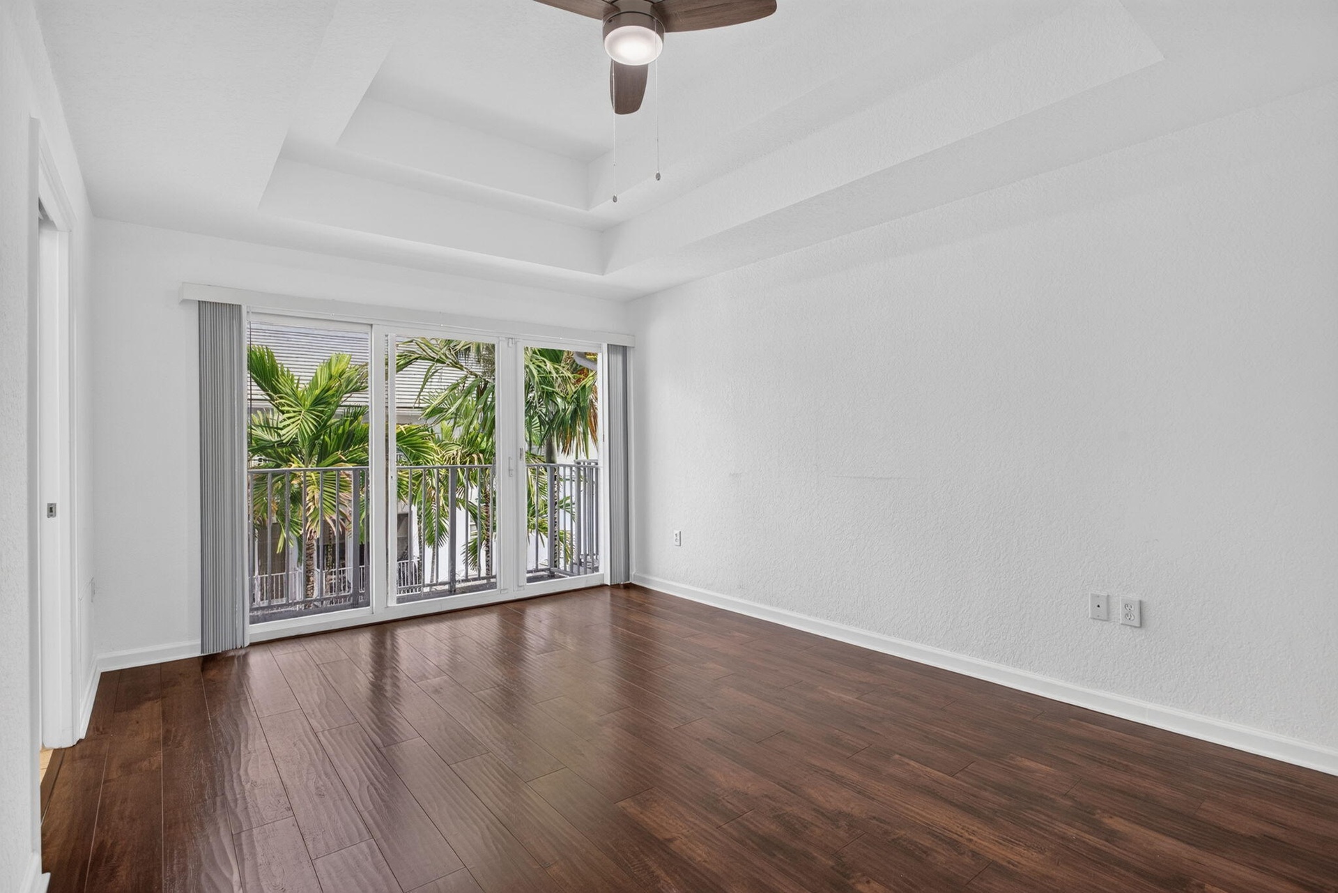Dark wood-finish flooring with a tray ceiling and ceiling fan