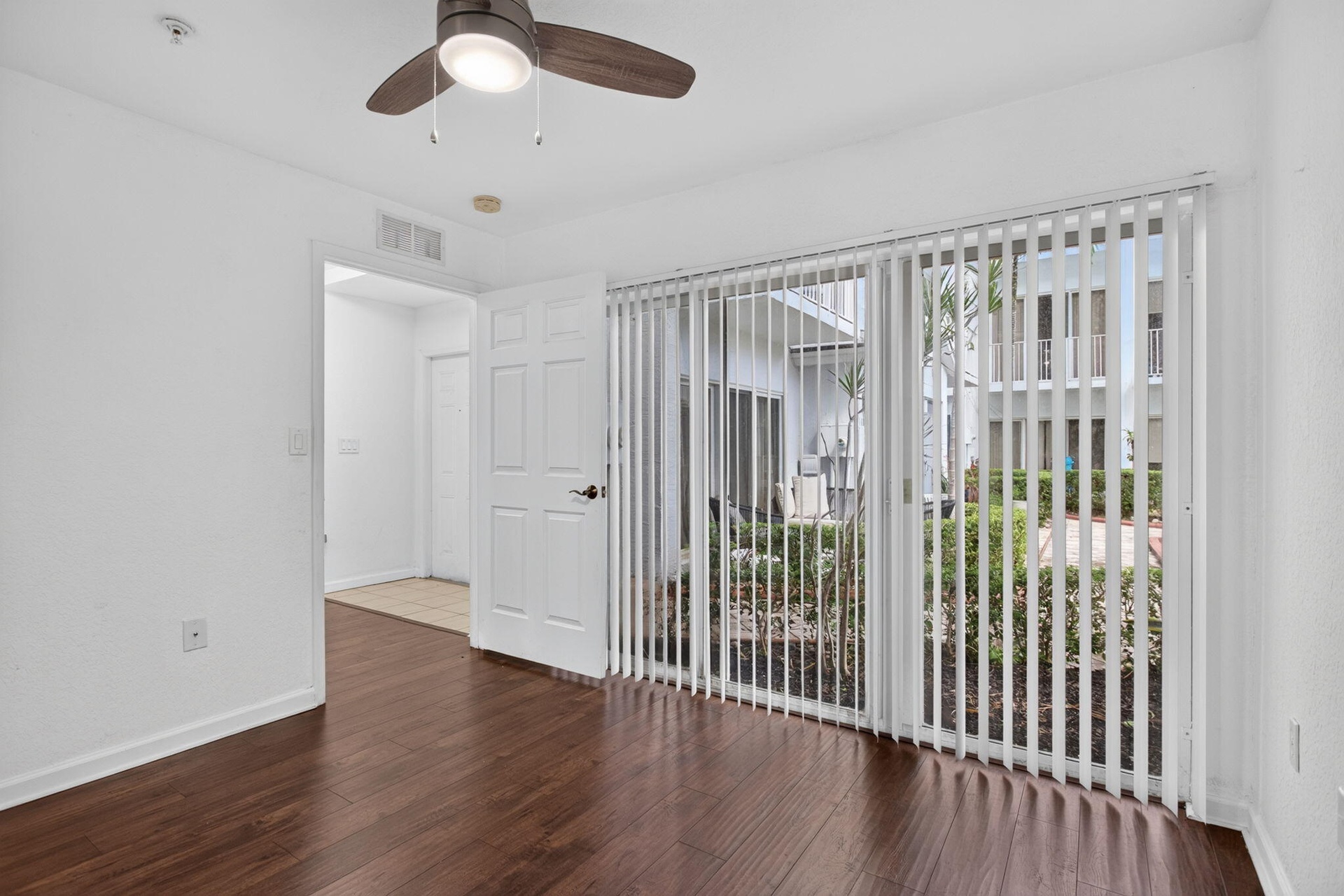 Wood-finish flooring, ceiling fan with integrated lighting, and full-height vertical blinds