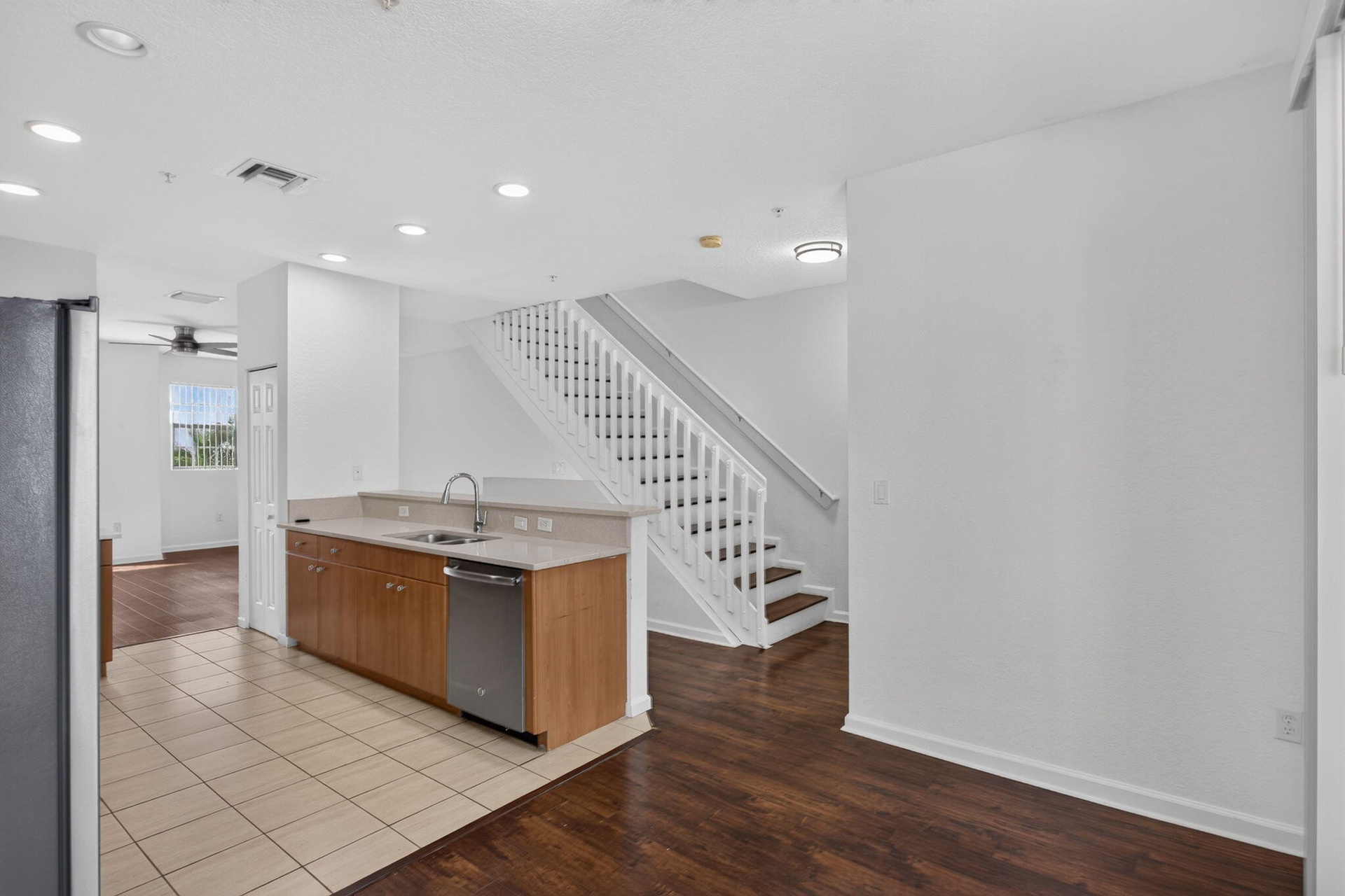 Kitchen with wood-finish cabinetry, stainless steel dishwasher, and light-toned countertops