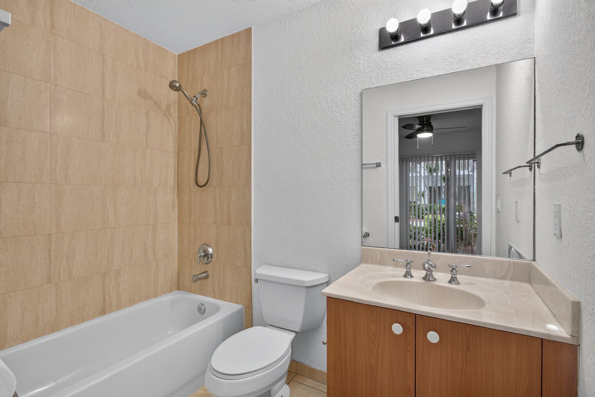 Bathroom featuring a tub/shower combination with light-toned wall tiling, a vanity with a light-colored countertop, and a built-in wood-finish cabinet