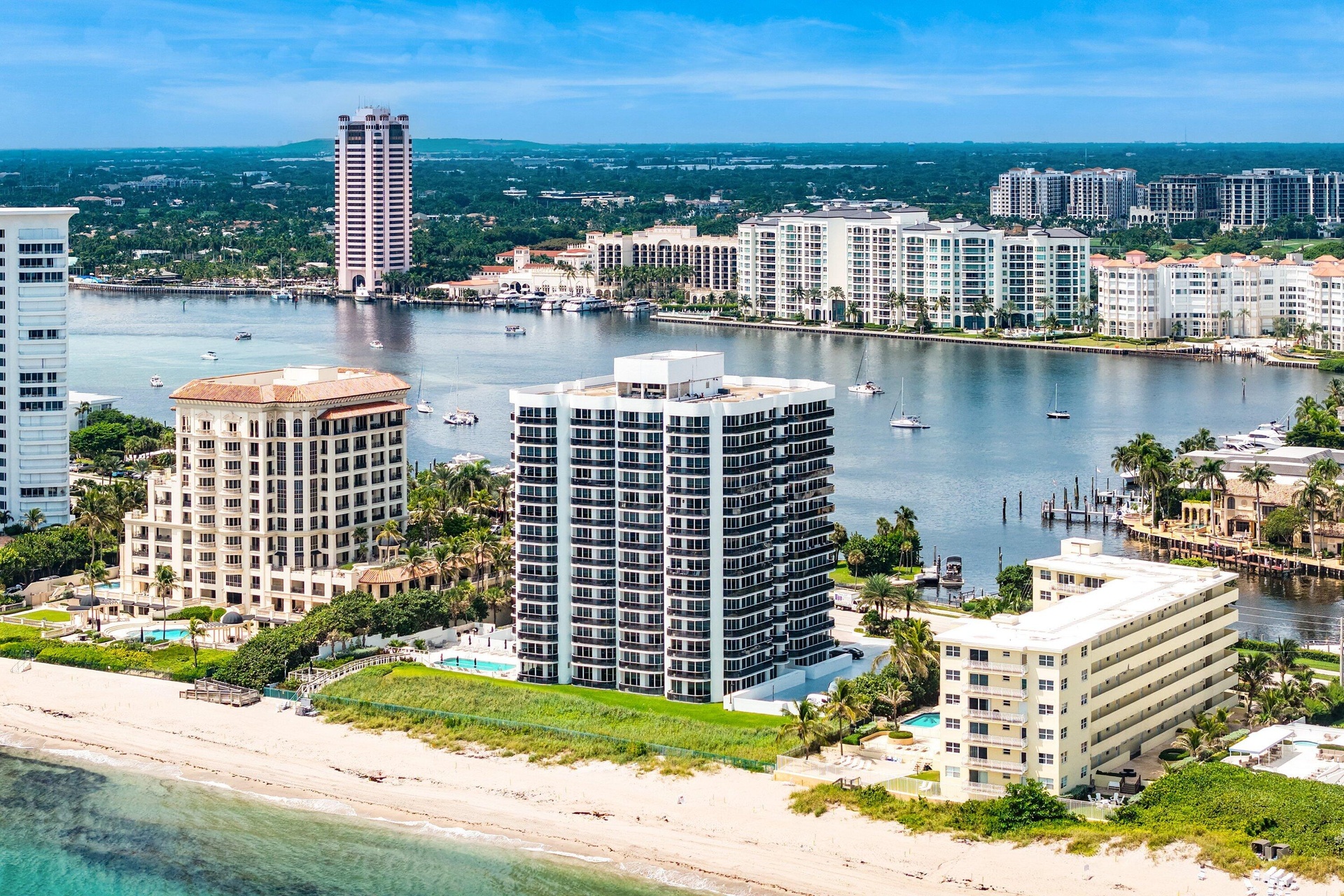 Coastal setting featuring a sandy beach, multiple residential towers, and a prominent waterway with several boats