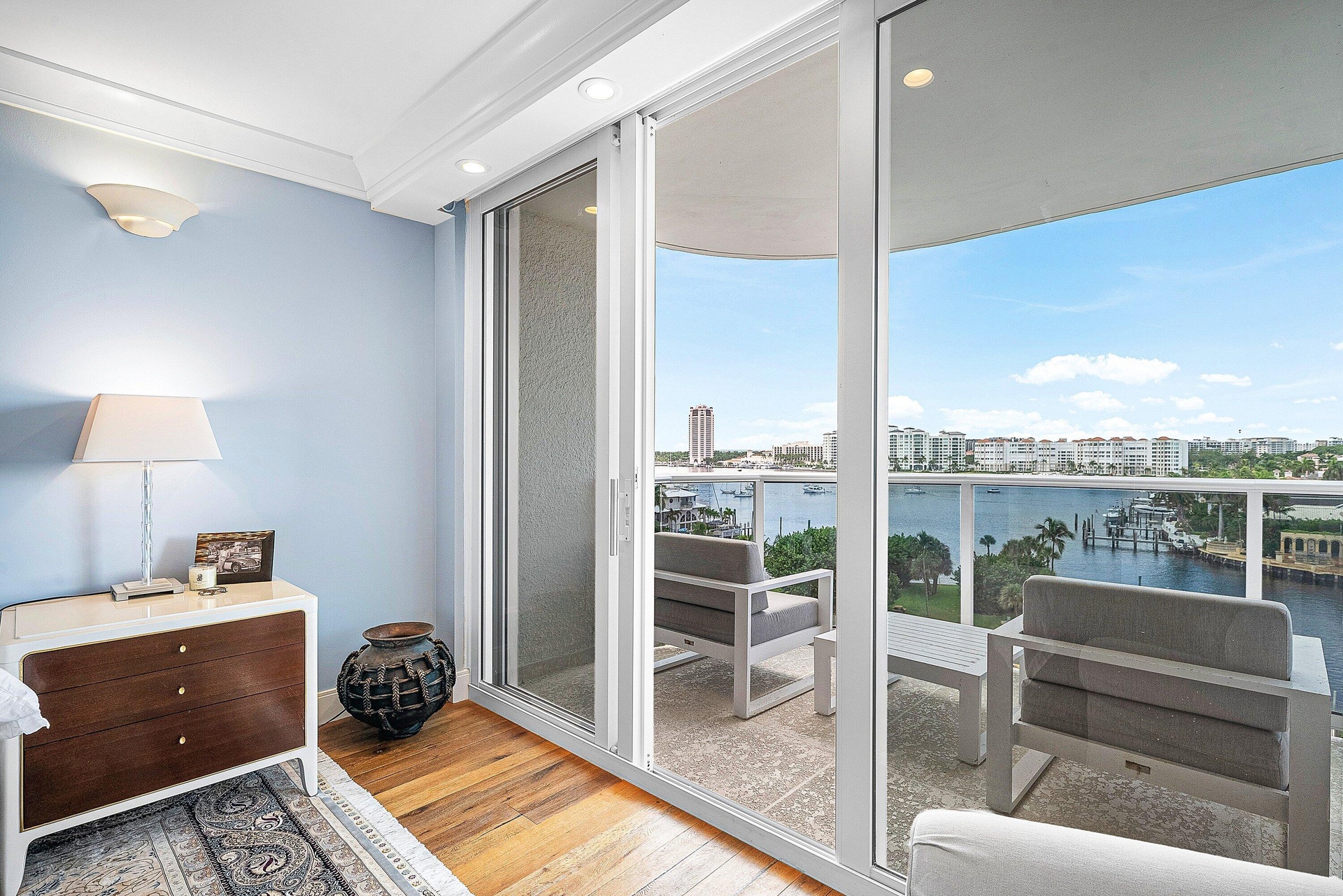Sliding glass doors opening to a private balcony with glass railings, providing an expansive water backdrop