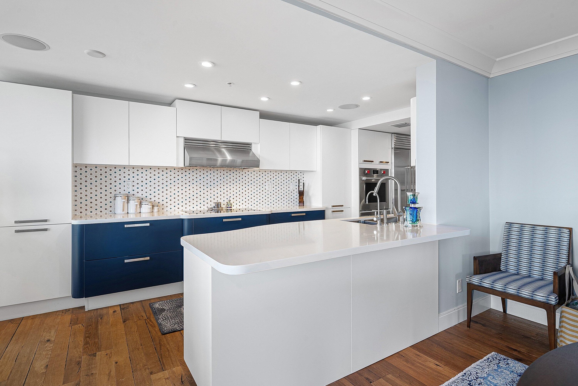 Modern kitchen featuring white and blue cabinetry, a patterned tile backsplash, stainless steel range hood, recessed lighting, and wood-finish floorin