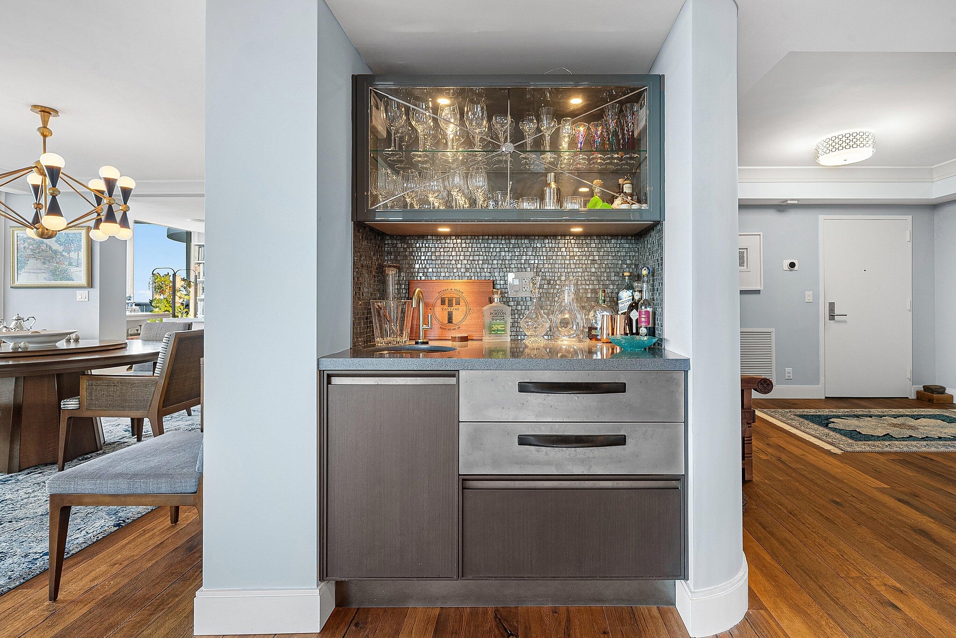 Built-in wet bar with a tiled backsplash, upper illuminated glass cabinetry, integrated under-counter storage, and wood-finish flooring