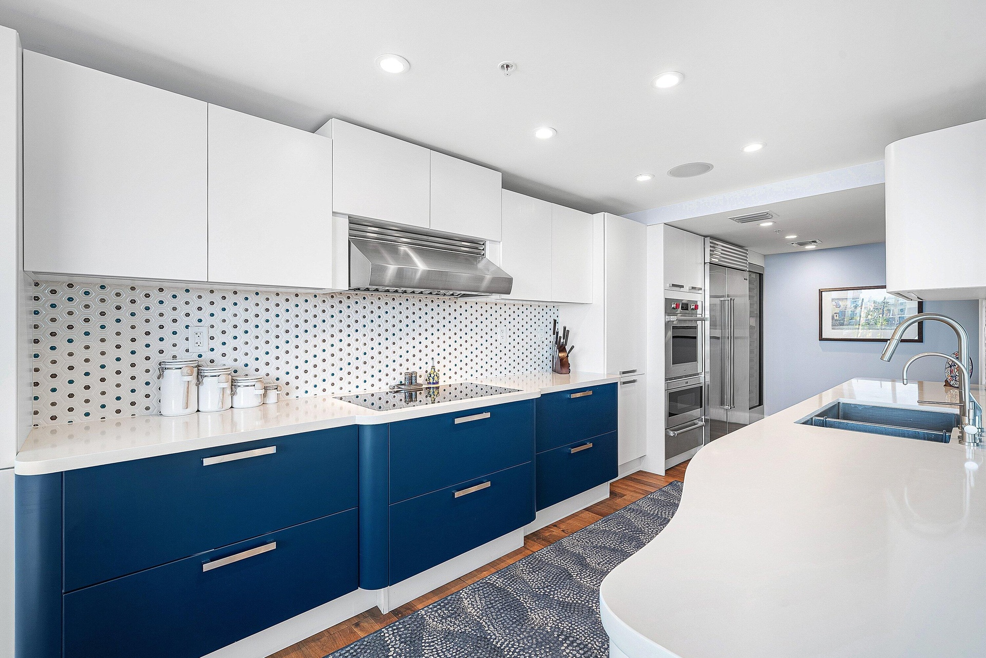 Kitchen featuring white upper cabinetry, blue lower cabinetry, hexagonal patterned backsplash, stainless steel appliances, and an integrated kitchen i