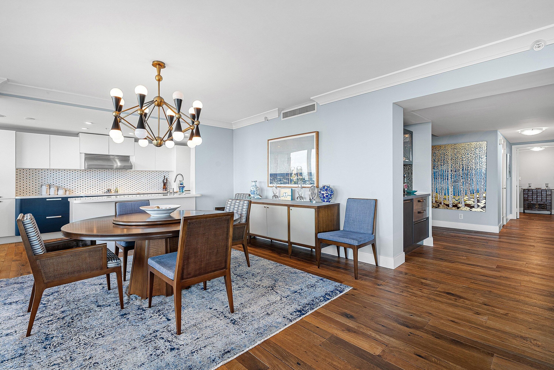 Wood-finish flooring, recessed lighting, crown molding, white cabinetry, and a geometric chandelier