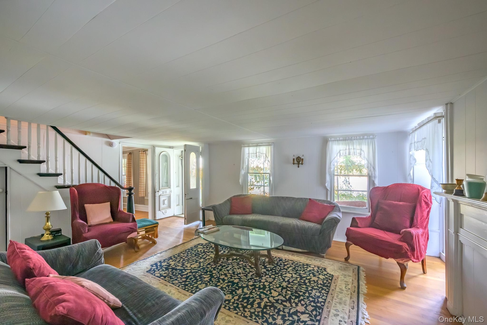 Hardwood flooring, painted white walls, white paneled ceilings, white fireplace mantel, and a staircase with dark wood handrails