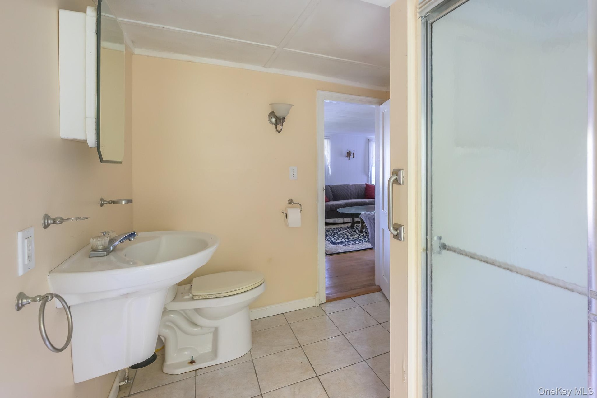 Pedestal sink, ceramic tile flooring, wall-mounted medicine cabinet, and a shower enclosure with frosted glass