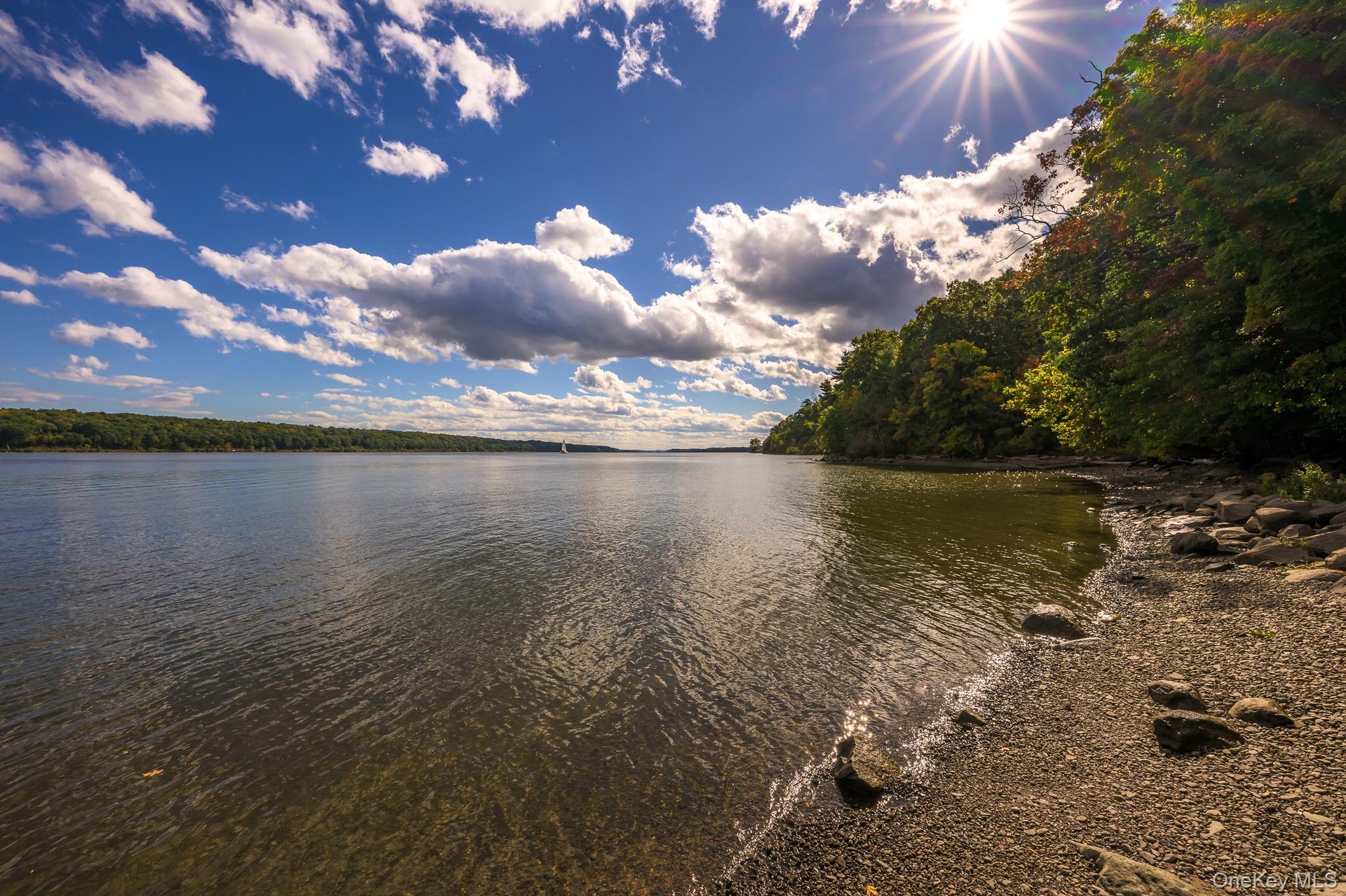 Shoreline property featuring a natural pebble beach and mature trees bordering the water