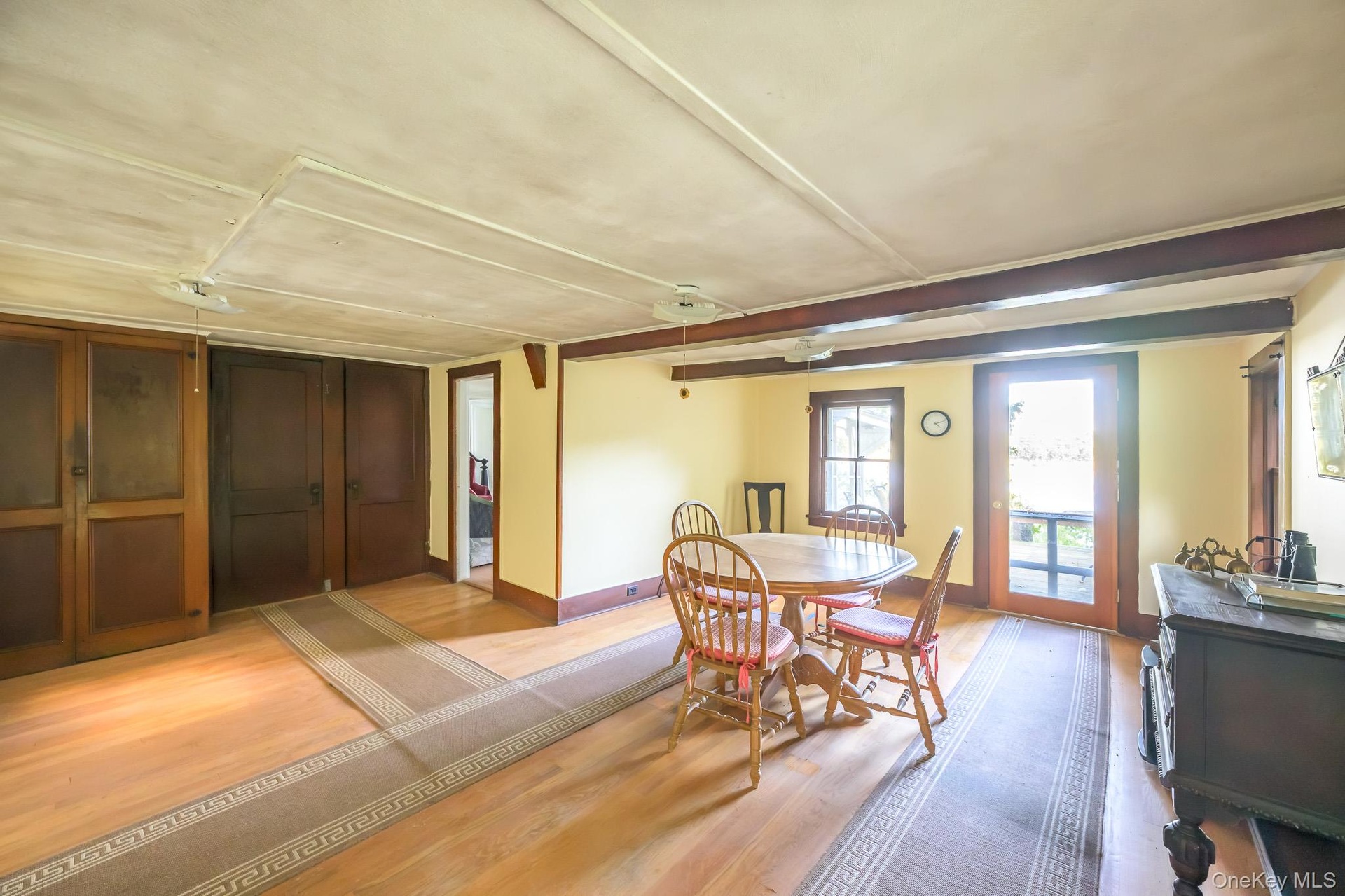 Hardwood flooring throughout, exposed ceiling beams, built-in wooden cabinetry, single-pane window with wooden frame, and a glass-paneled exterior doo