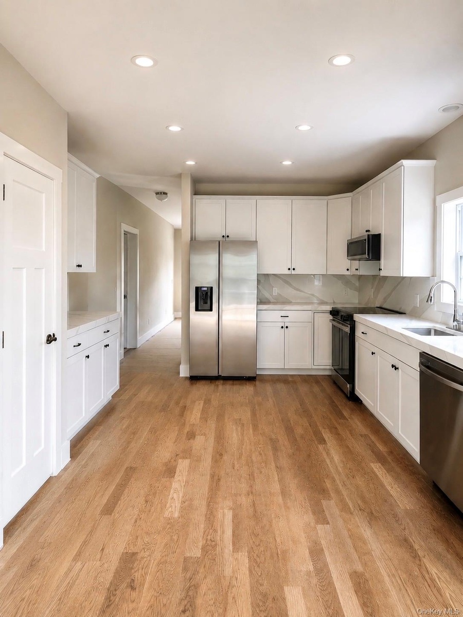 Open-concept kitchen featuring wood-finish flooring, white cabinetry, stainless steel appliances, white countertops, and recessed lighting