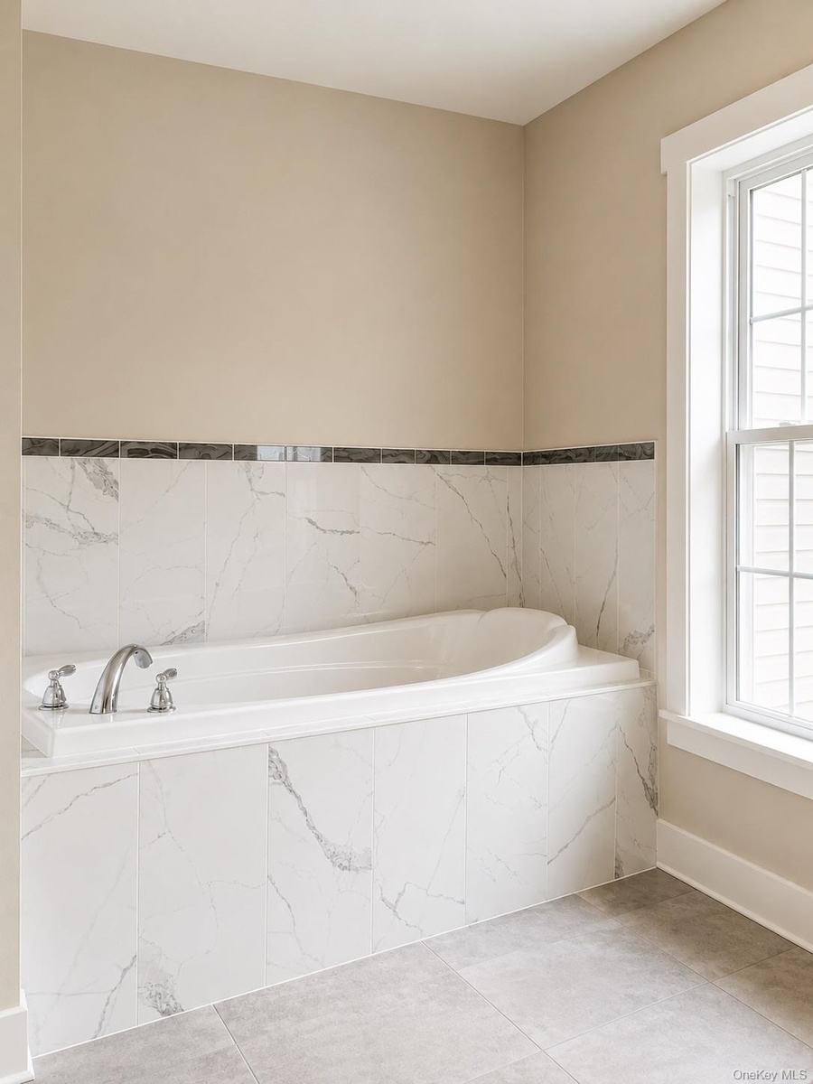 Soaking tub with chrome fixtures, surrounded by white marble-look tile