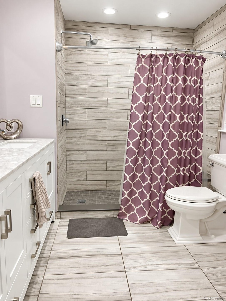 Walk-in shower with wood-look tile surround, tiled flooring, built-in vanity with white cabinetry, and a white countertop