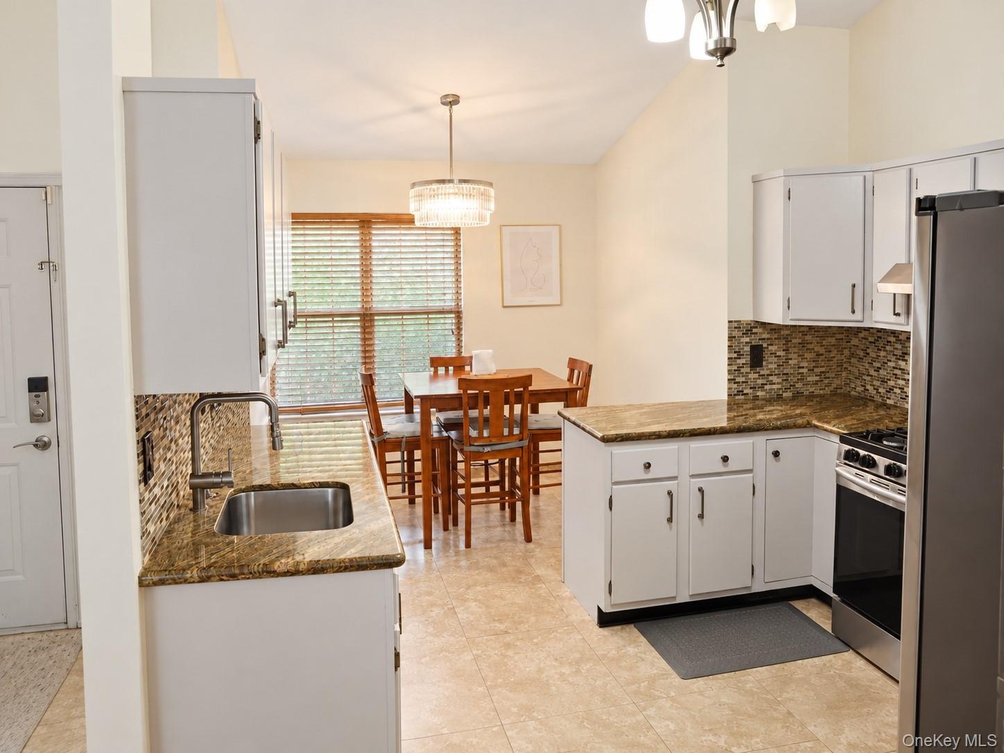 Kitchen featuring white cabinetry, stone countertops, mosaic tile backsplash, stainless steel appliances, and tile flooring
