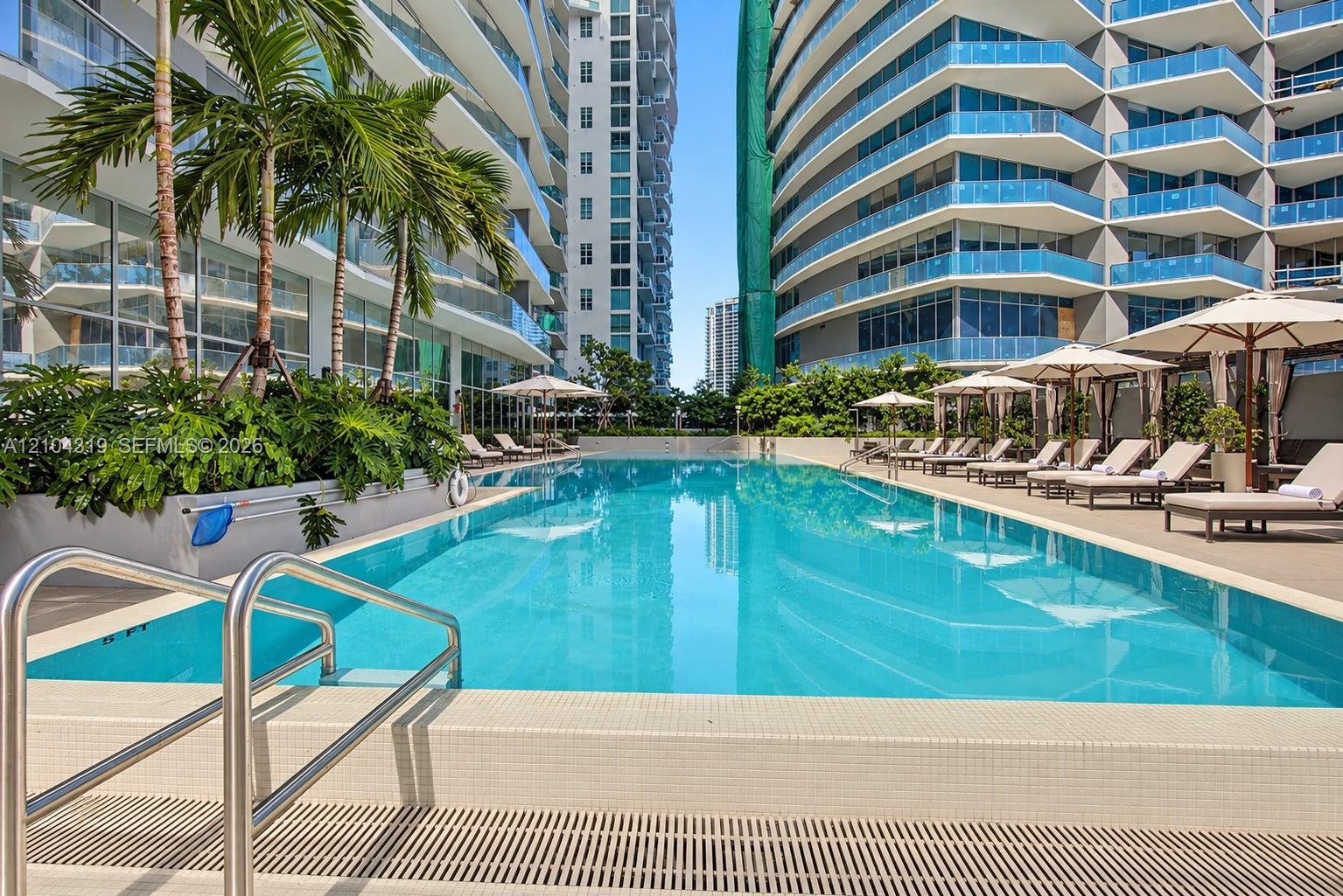 Swimming pool featuring a tiled perimeter, stainless steel entry rails, integrated landscaping, and paved poolside decking