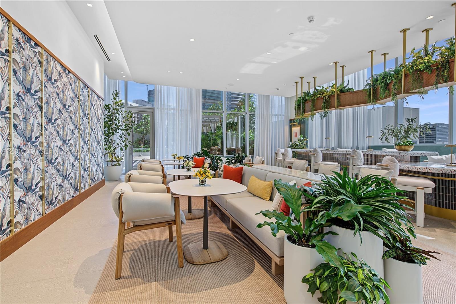 Common area featuring floor-to-ceiling windows, patterned wall covering with brass trim, a built-in stone-top bar, and suspended metal shelving
