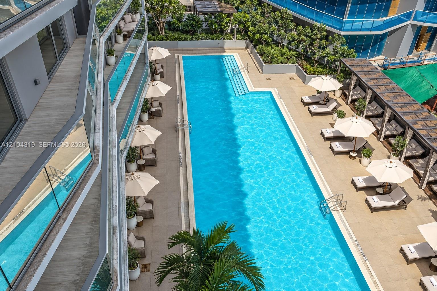 Rectangular swimming pool featuring integrated steps and stone-paved decking, complemented by a shaded pergola structure and landscaped perimeter gree