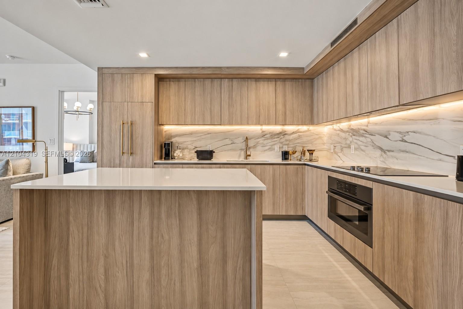 Kitchen featuring custom wood-finish cabinetry, a white stone island countertop, integrated appliances, and a full-height stone backsplash with under-