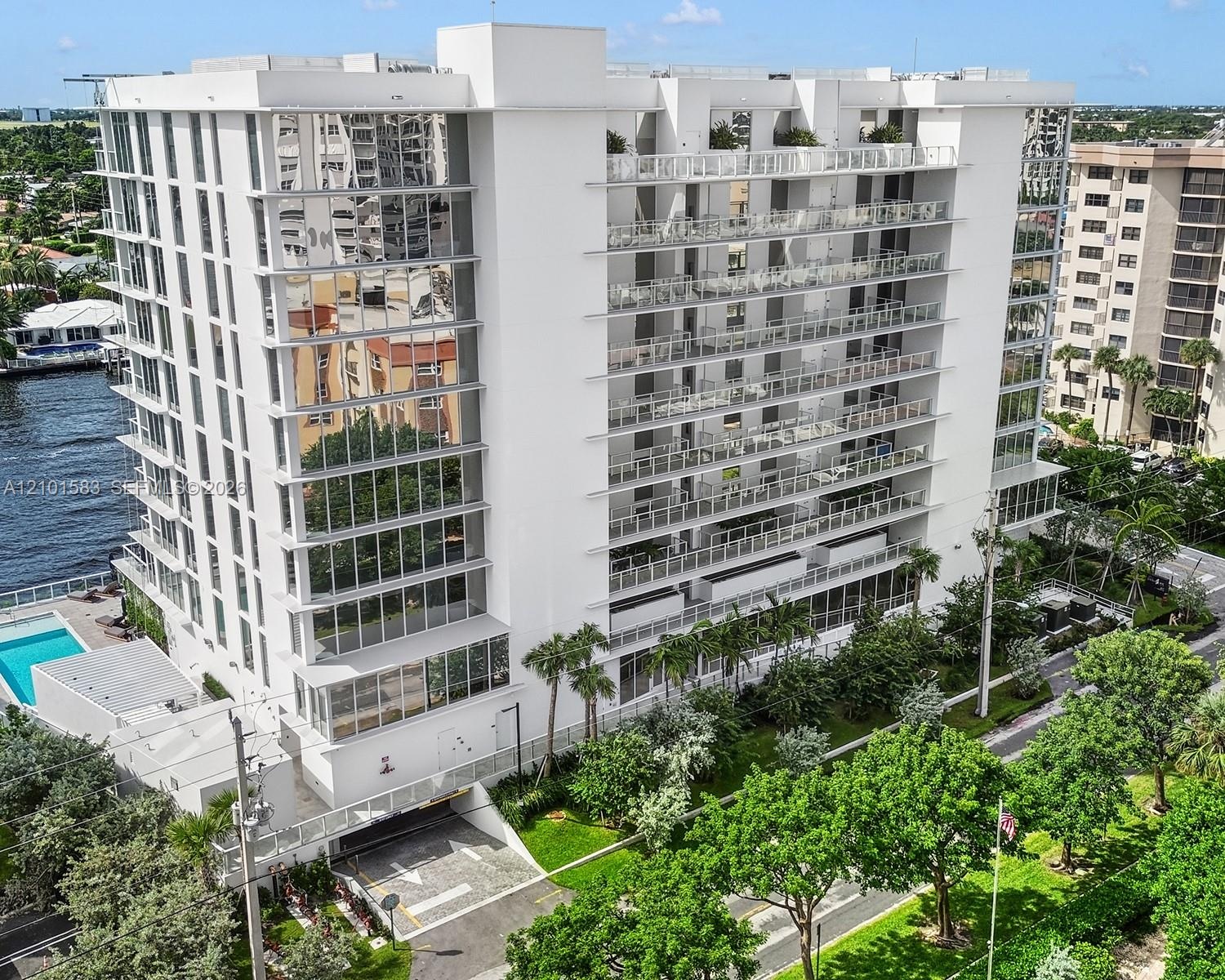 Multi-story residential building featuring floor-to-ceiling glass paneling, tiered cantilevered balconies with glass railings, an attached swimming po