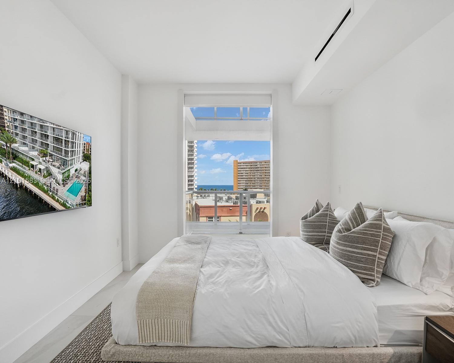 Floor-to-ceiling window featuring a glass balcony railing, neutral tile flooring, wall-mounted ductless climate control, and prominent water and citys