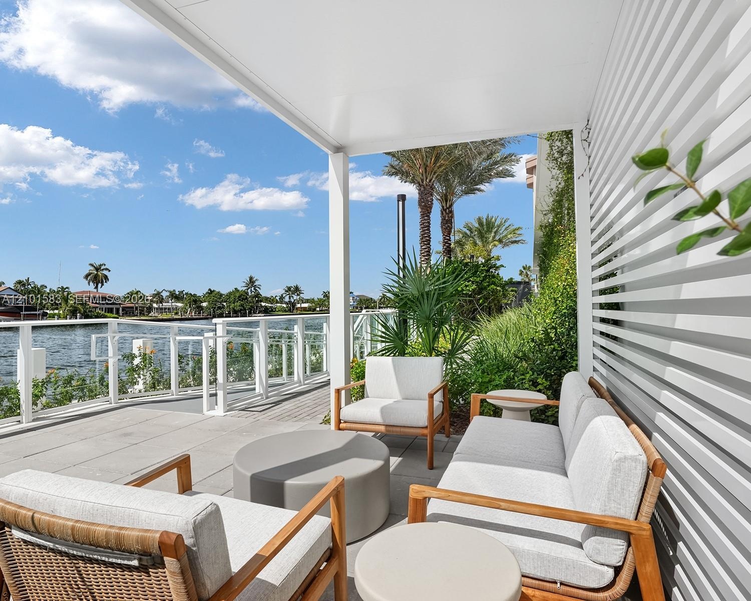 Covered patio featuring concrete tile flooring, horizontal slat privacy screen, and a glass-paneled railing overlooking the water