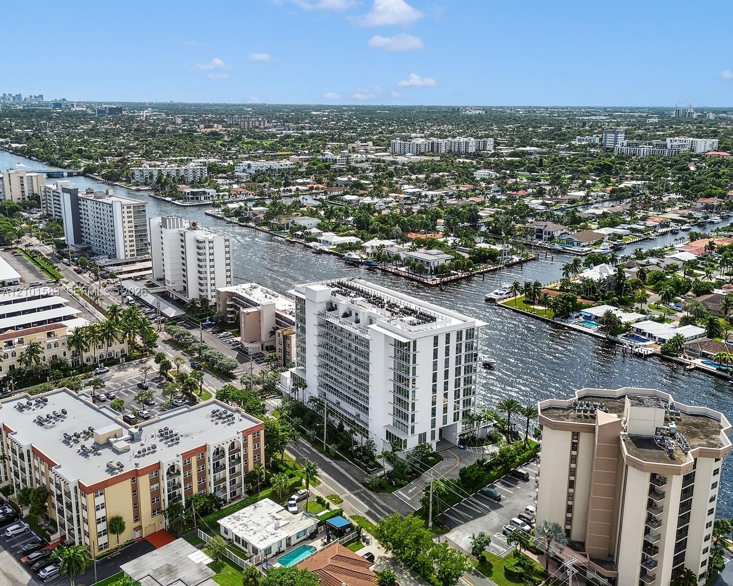 Aerial perspective of a high-rise residential structure positioned along a deep-water canal, featuring expansive balconies, concrete building construc
