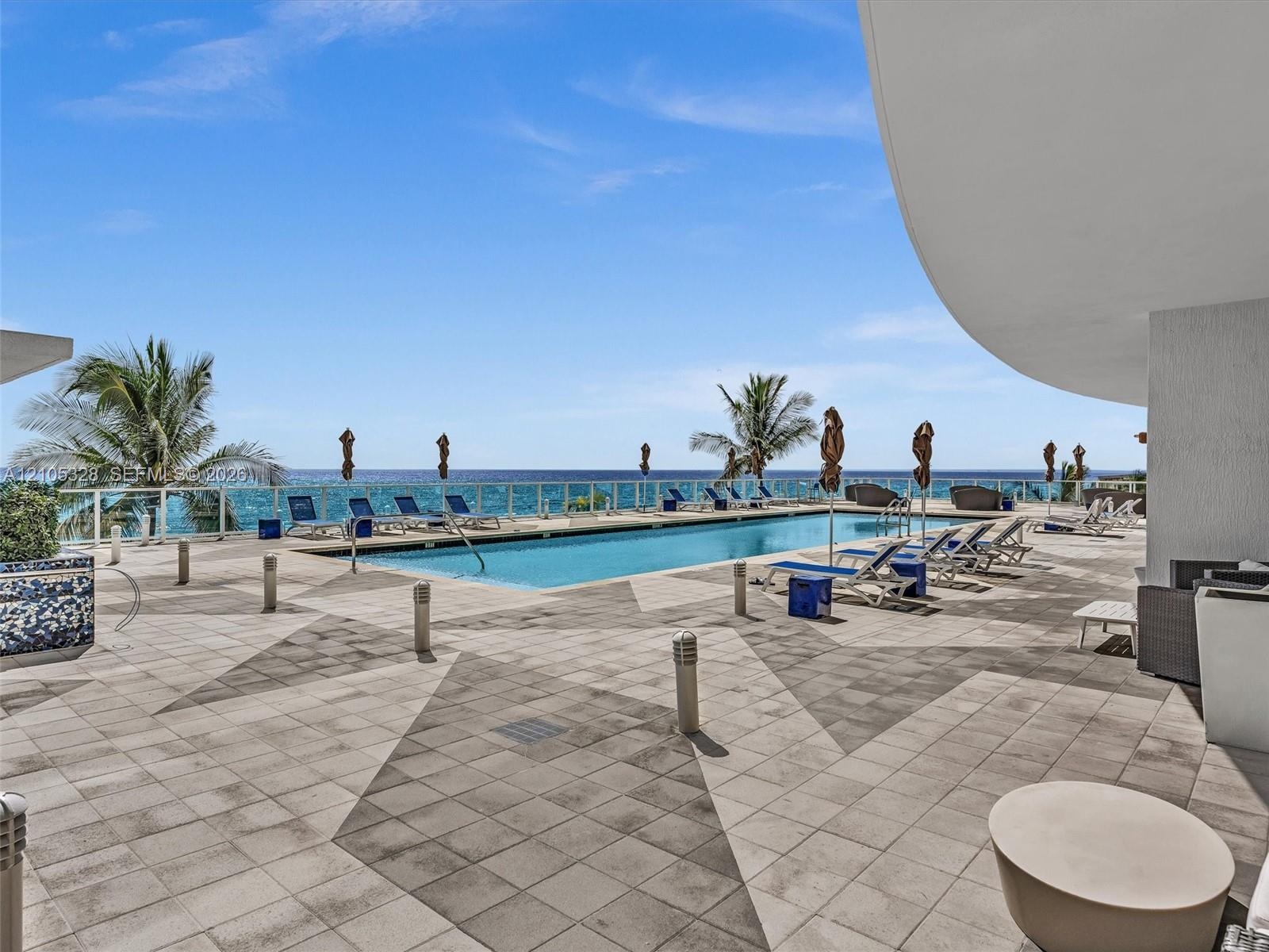 Experience oceanfront resort-style living at Apogee Beach, featuring an inviting swimming pool, expansive pool deck, sleek glass railings, and direct 