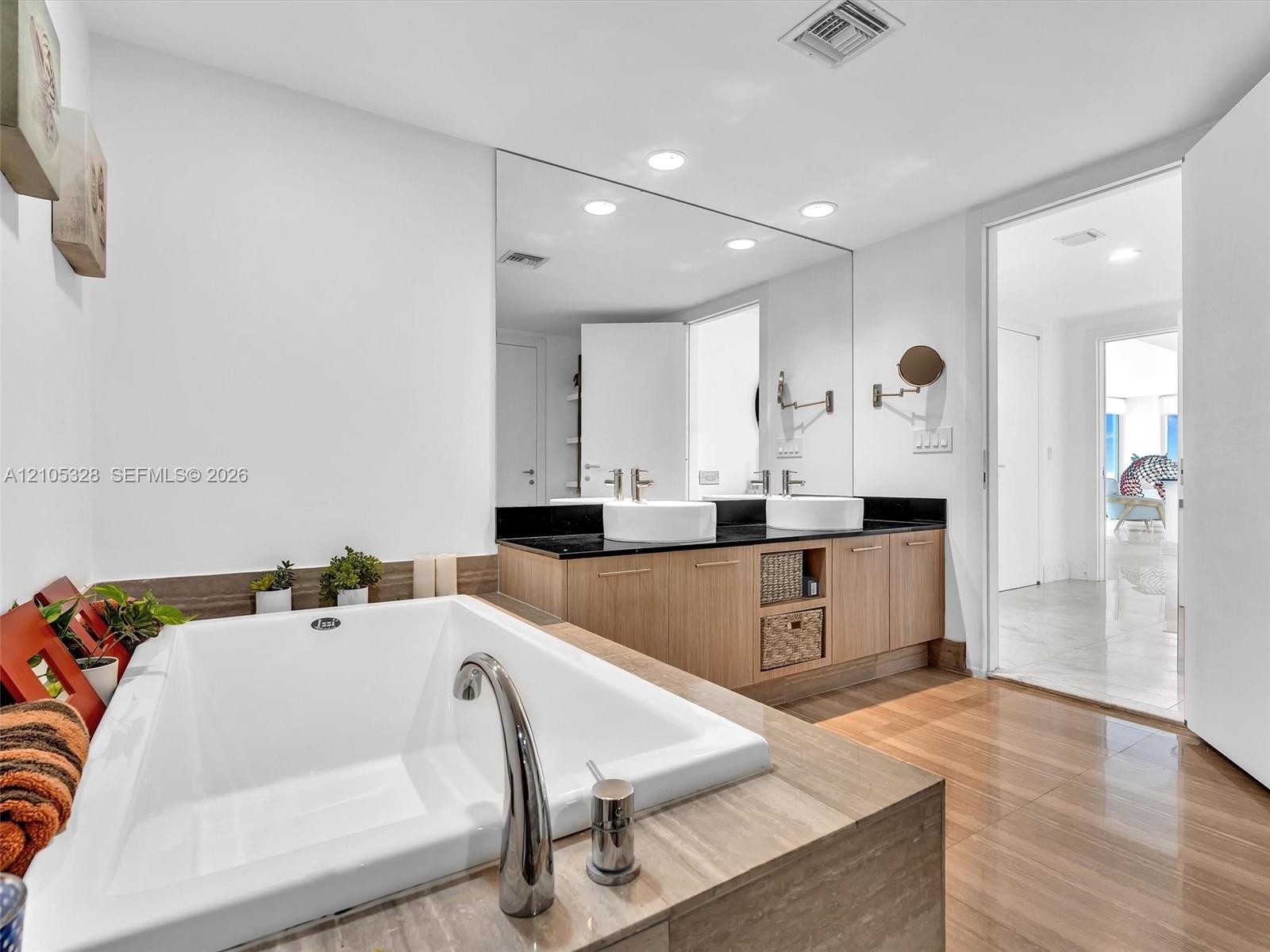 Luxurious spa-inspired bathroom featuring dual vessel sinks, an expansive vanity with built-in storage, a full-width mirror, a soaking tub, and a sepa