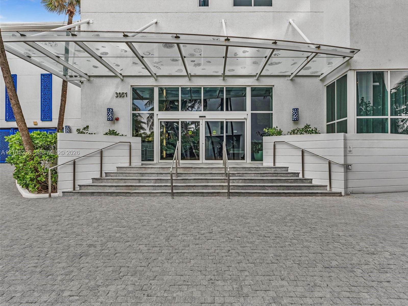 Elegant building entrance featuring a contemporary glass canopy, beautifully paved entryway, and sleek stainless steel railings, creating a sophistica