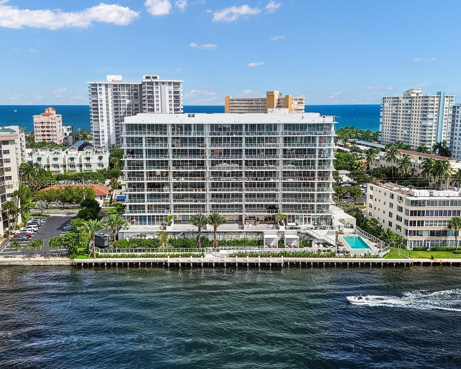 Waterfront multi-story residential building featuring floor-to-ceiling glass balconies, private dockage, a ground-level swimming pool, and manicured l