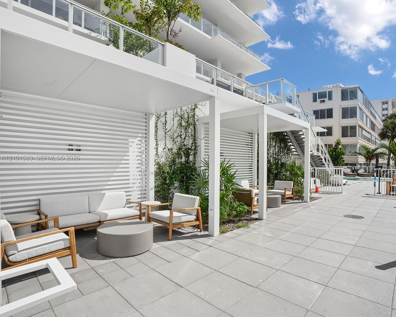 Outdoor terrace featuring a concrete paver patio, white aluminum pergolas, horizontal slat privacy walls, and glass-paneled balconies