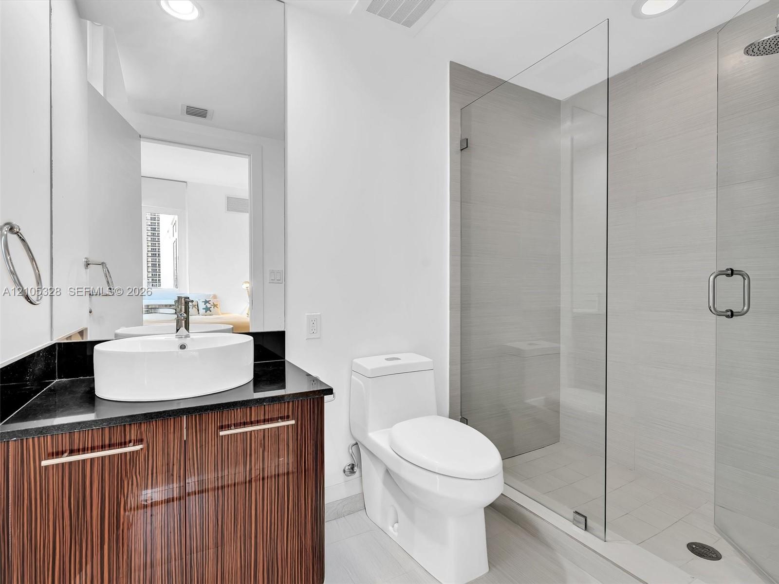 Elegant contemporary bathroom featuring a sleek vanity with warm finish cabinetry and a sophisticated dark countertop.