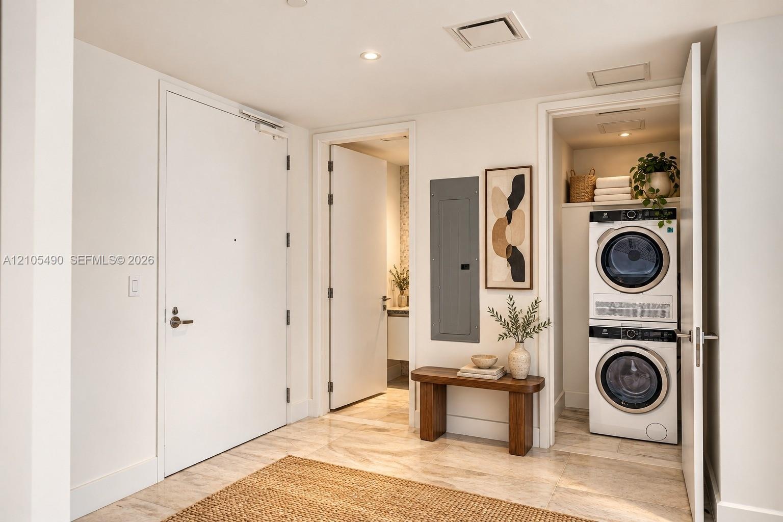 Neutral-toned stone flooring and recessed ceiling lighting throughout, featuring a dedicated laundry closet with a stacked washer and dryer, solid-cor