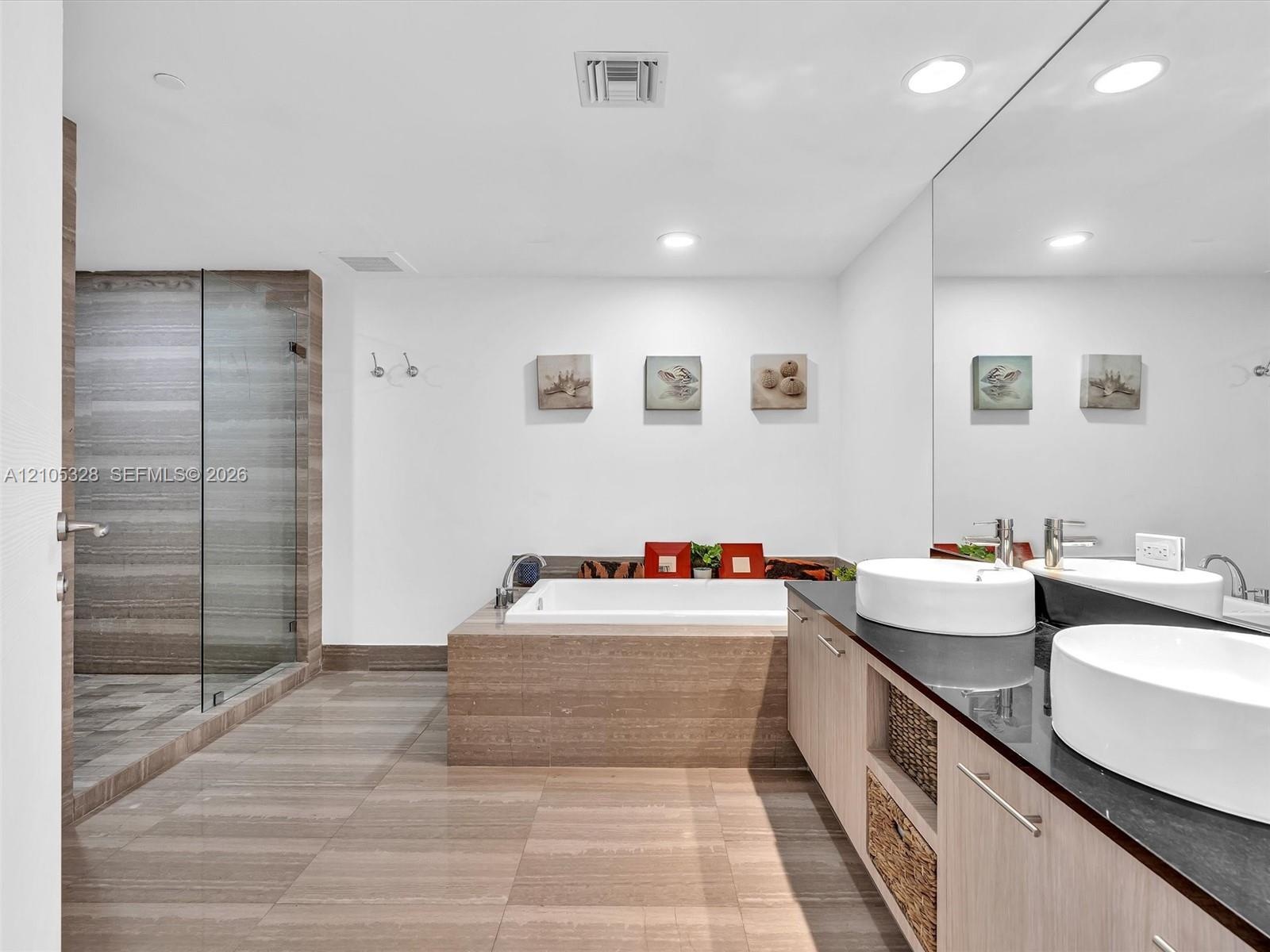 Luxurious spa-inspired bathroom featuring dual vessel sinks, an expansive vanity with built-in storage, a full-width mirror, a soaking tub, and a sepa