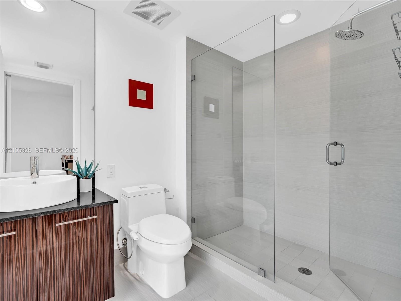 Elegant contemporary bathroom featuring a sleek vanity with warm finish cabinetry and a sophisticated dark countertop.