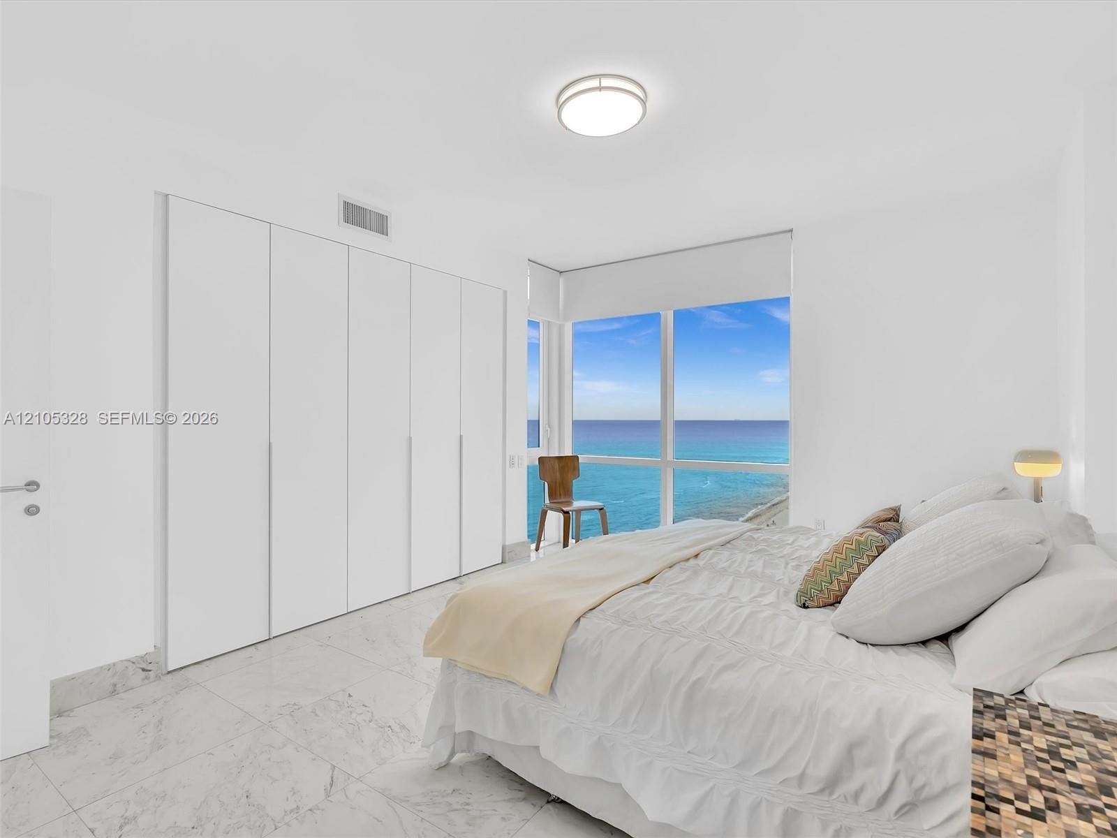 Bright and elegant bedroom featuring dramatic floor-to-ceiling windows, custom built-in wardrobe cabinetry, luxurious marble-look flooring, recessed c