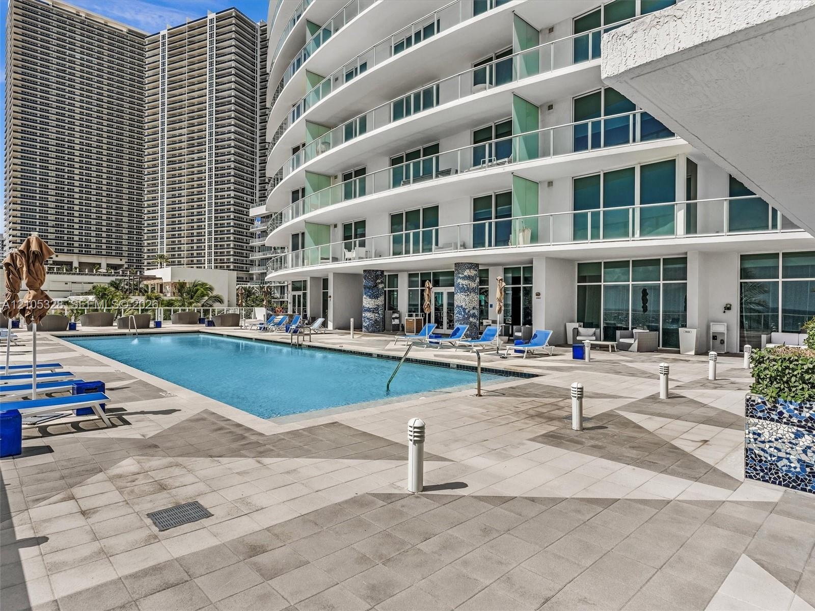 Experience oceanfront resort-style living at Apogee Beach, featuring an inviting swimming pool, expansive pool deck, sleek glass railings, and direct 