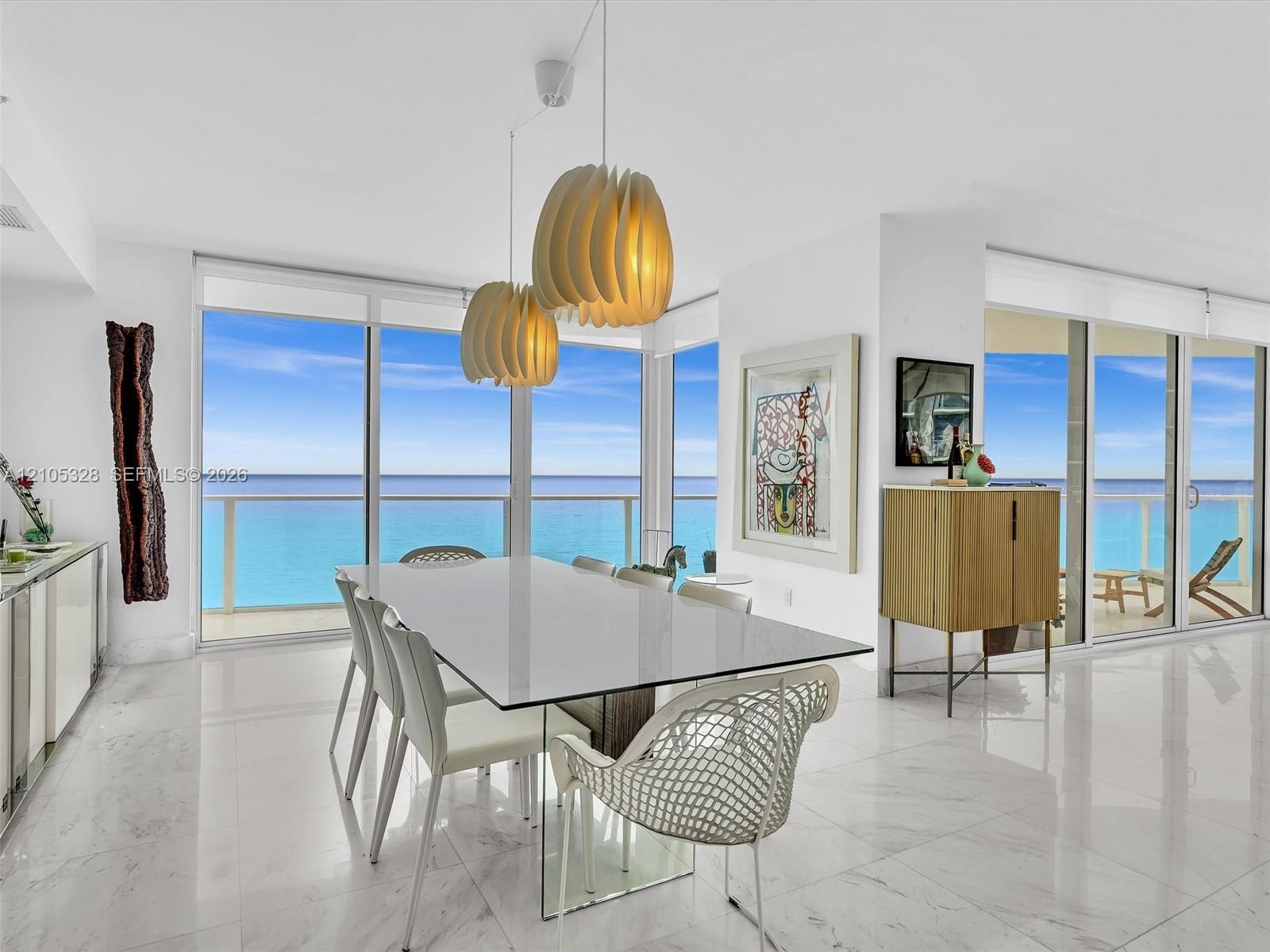 Elegant dining area featuring floor-to-ceiling glass doors and windows, large-format tile flooring, contemporary pendant lighting, and a glass-top din