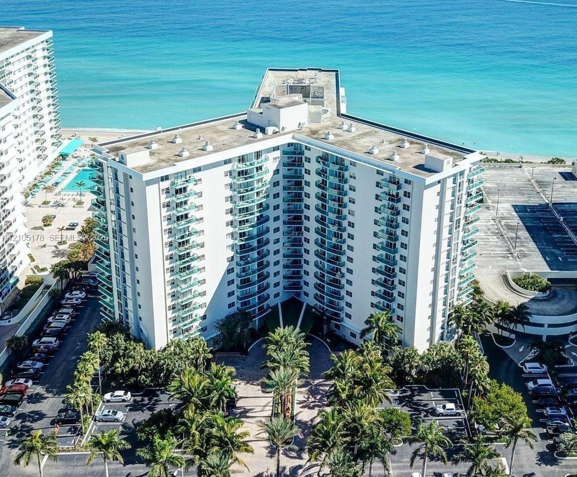 High-rise residential structure featuring tiered balconies, a paved circular entryway, and extensive tropical landscaping