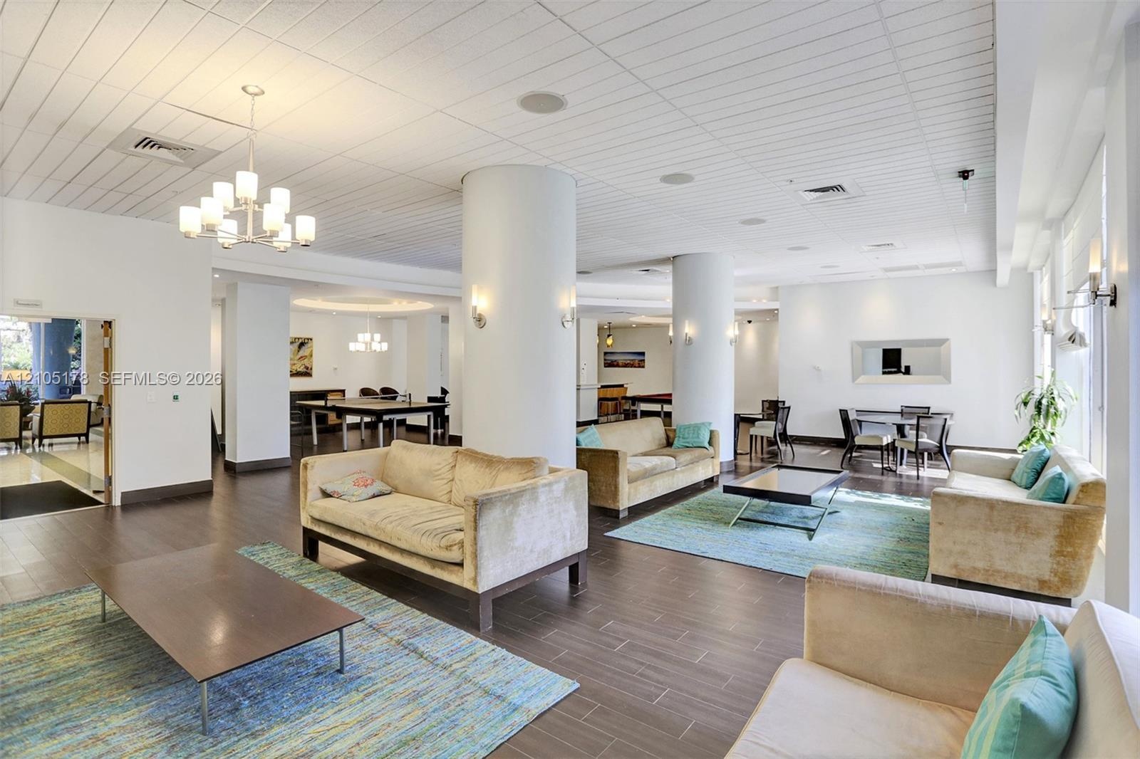Open-concept interior featuring structural cylindrical columns, wood-finish plank flooring, recessed ceiling lighting, and multi-arm chandelier fixtur