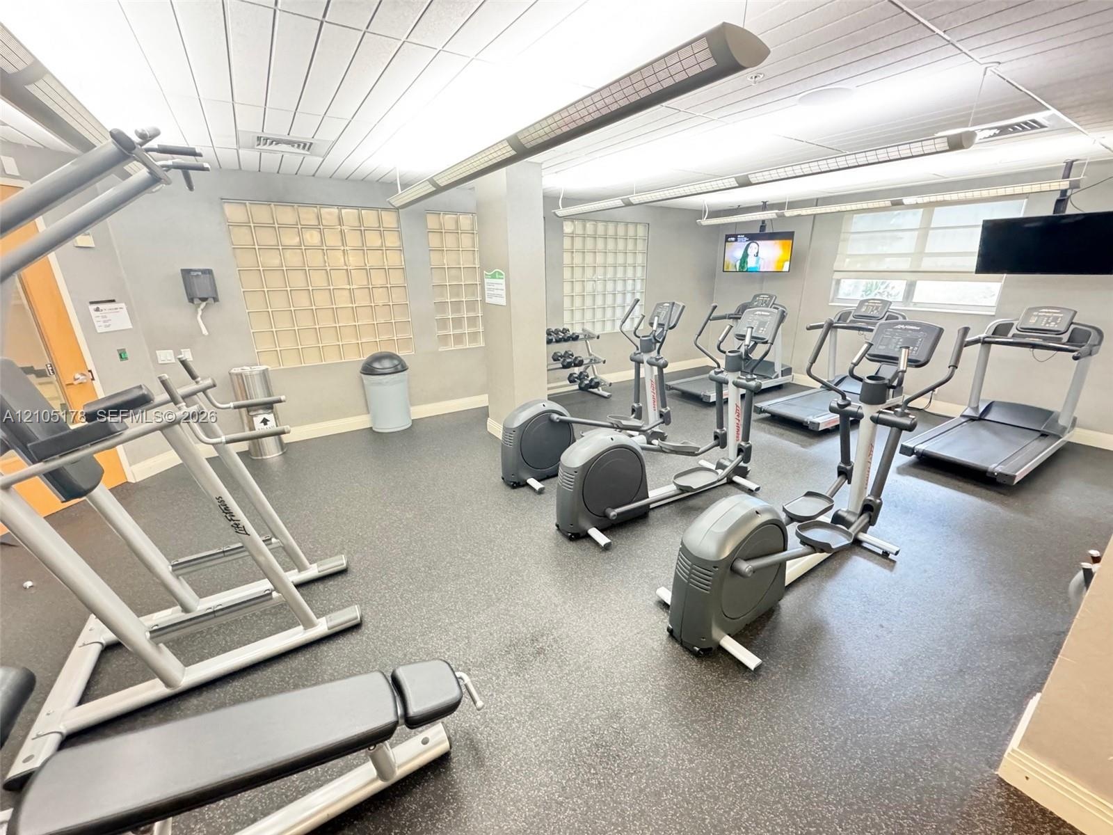 Fitness center featuring textured rubber flooring, panelized drop ceiling, glass block windows, and linear overhead lighting